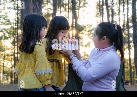 Bonne mère et enfants pique-nique s'asseoir près d'un poêle et griller un barbecue dans la forêt de pins, manger et avoir la conversation. Bonne famille en vacances Banque D'Images