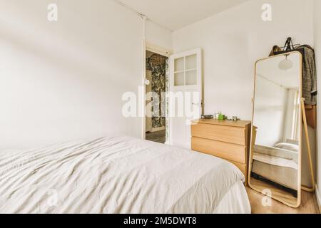 une chambre avec un lit, une commode et un miroir sur le mur à côté des placards de l'autre chambre Banque D'Images
