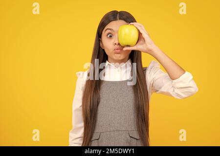 Visage amusant. Enfant fille mangeant une pomme sur fond jaune isolé. Tennager avec des fruits. Banque D'Images