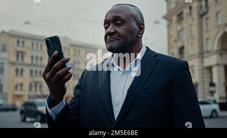 Adulte africain homme d'âge mûr travailleur Manager entrepreneur d'âge moyen homme d'affaires senior à l'extérieur dans la ville avec téléphone parler vidéo appeler des affaires sérieuses Banque D'Images