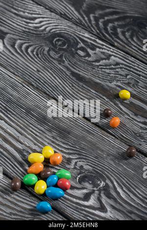 Bonbons au chocolat en glaçure multicolore. Éparpillées sur des planches de pin noir. Banque D'Images