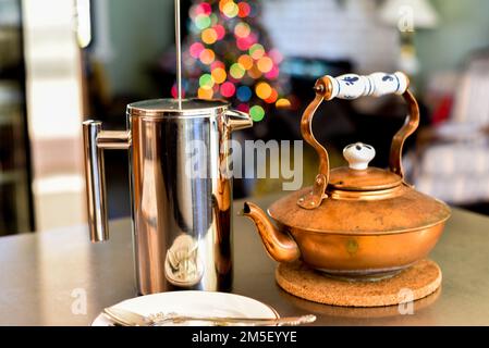 Presse française en acier inoxydable, et bouilloire à thé en cuivre sur une table en bois le matin de Noël avec de jolies lumières de Noël floues dans le Banque D'Images