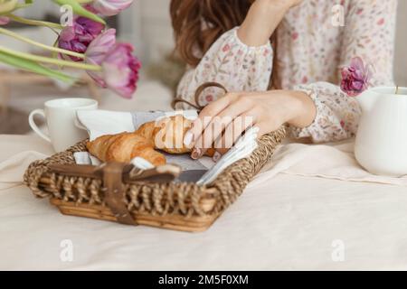 Croissants frais dans un panier en osier sur la table à côté d'un vase de tulipes lilas Banque D'Images