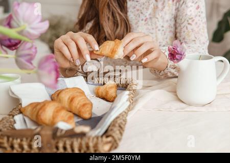 Croissants frais dans un panier en osier sur la table à côté d'un vase de tulipes lilas Banque D'Images