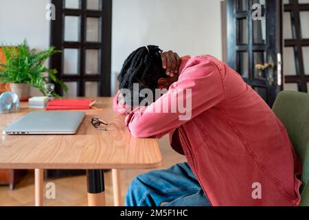 Un homme afro-américain souffrant débilé qui se labourait la tête au-dessus d'un bureau tenant le cou ressent de la douleur Banque D'Images