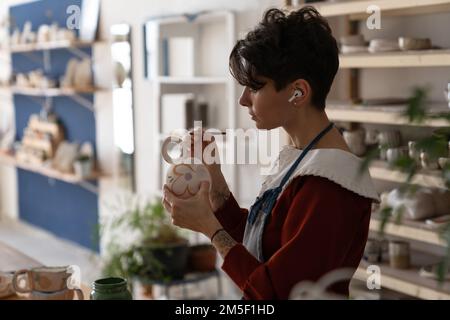 Artiste italienne concentrée utilisant la brosse applique de la peinture sur des plats faits à la main en argile naturelle Banque D'Images