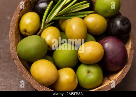 Olives multicolores et une branche de romarin dans une coquille de noix de coco. Gros plan. Banque D'Images