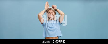 Studio de divertissement insouciant et émouvant femme de charme heureuse avec des tatouages sur les bras agissant comme un lapin avec les paumes sur la tête se fait joies Banque D'Images