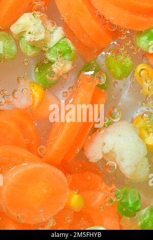 Faire bouillir de l'eau avec des légumes frais, gros plan. Vue rapprochée de la soupe de légumes avec carottes, petits pois, chou-fleur et maïs en fond d'eau. Texte Banque D'Images