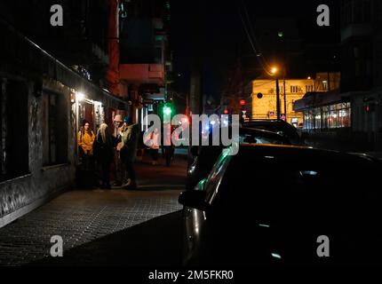 Kiev, Ukraine. 26th décembre 2022. Les gens boivent du café devant un café dans une rue sombre pendant une panne de courant à Kiev. L'armée russe a mené des attaques massives de roquettes et de drones kamikaze sur les infrastructures énergétiques ukrainiennes. Après de graves dommages au réseau électrique dans de nombreuses villes d'Ukraine, la compagnie nationale d'électricité Ukrenergo a introduit des coupures d'électricité d'urgence et toutes les heures. Crédit : SOPA Images Limited/Alamy Live News Banque D'Images