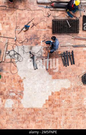 La photo aérienne de deux hommes en uniforme gris et bleu est le métal de soudage à l'arc avec machine à souder au sol sur le chantier. Banque D'Images