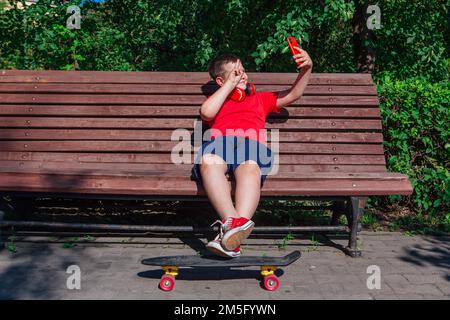 Garçon assis sur le banc et communique par chat vidéo à l'aide d'un smartphone et d'Internet. Banque D'Images