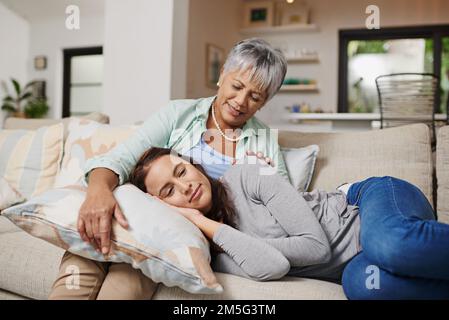 Rien n'est plus confortable que les mamans. une jeune femme se reposant avec sa tête sur les genoux de ses mères dans le salon. Banque D'Images