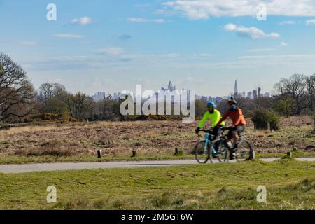 Deux cyclistes dans un parc passent devant une toile de fond étonnante des bâtiments du centre de Londres Banque D'Images