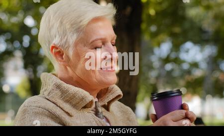 Visage ridé de 60s heureuse femme âgée à l'extérieur dans le parc regardant de côté ayant le grand sourire, implants dentaires et prothèses satisfait portrait de client Banque D'Images