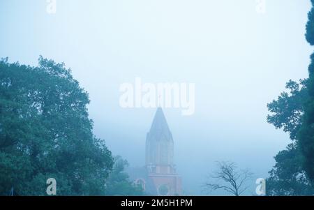 Vue panoramique sur la tour de l'église avec croix entourée d'arbres verts entourés d'un épais brouillard Banque D'Images