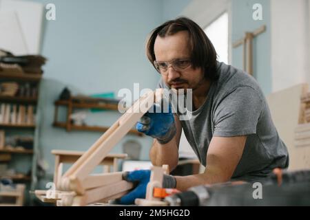 Un charpentier fabrique des jouets en bois dans un atelier de menuiserie. Faire un carrousel de lit. Banque D'Images