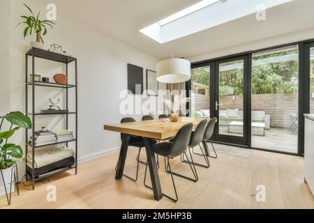 une salle à manger avec parquet et portes en verre qui s'ouvrent sur le patio de l'arrière-cour, qui est entouré d'arbres Banque D'Images