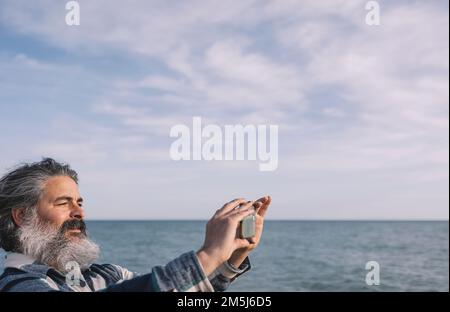 Joyeux barbu qui prend un selfie ou une photo avec un smartphone sur la plage Banque D'Images