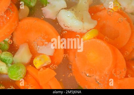 Gros plan de la soupe de légumes frais avec carottes, petits pois, chou-fleur et maïs sur fond blanc. Potez les légumes avec des carottes, des pois, du chou-fleur et du maïs Banque D'Images