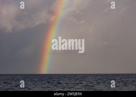 Un arc-en-ciel lumineux, causé par la lumière du soleil se réfractant à travers les gouttelettes d'eau, apparaît au-dessus de l'océan Pacifique Sud pendant la saison de la mousson. Banque D'Images