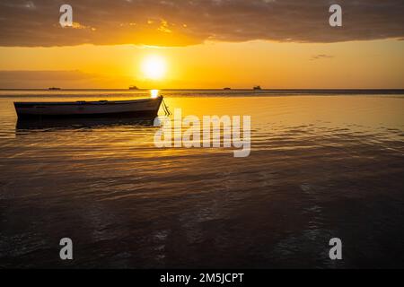 Baie-du-Tombeau Ile Maurice coucher de soleil sur la baie avec un seul bateau de pêche en avant-plan et à l'horizon montrant des cartes de pêche à grande échelle silhouetées Banque D'Images