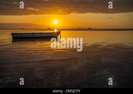 Baie-du-Tombeau Ile Maurice coucher de soleil sur la baie avec un seul bateau de pêche en avant-plan et à l'horizon montrant des cartes de pêche à grande échelle silhouetées Banque D'Images