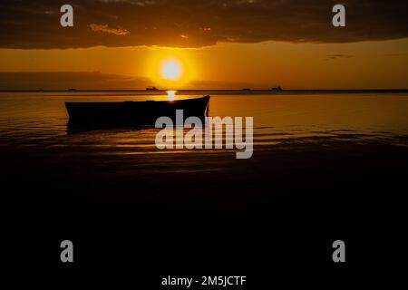 Baie-du-Tombeau Ile Maurice coucher de soleil sur la baie avec un seul bateau de pêche en avant-plan et à l'horizon montrant des cartes de pêche à grande échelle silhouetées Banque D'Images