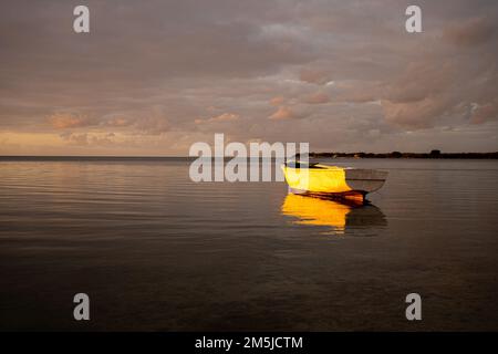 Baie-du-Tombeau Ile Maurice coucher de soleil sur la baie avec un seul bateau de pêche en avant-plan et à l'horizon montrant des cartes de pêche à grande échelle silhouetées Banque D'Images