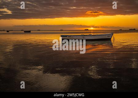 Baie-du-Tombeau Ile Maurice coucher de soleil sur la baie avec un seul bateau de pêche en avant-plan et à l'horizon montrant des cartes de pêche à grande échelle silhouetées Banque D'Images