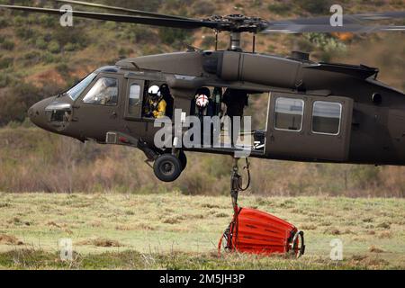 A ÉTATS-UNIS L'hélicoptère UH-60M Black Hawk de l'armée, piloté par des soldats du Bataillon des hélicoptères d'assaut 1st, 140th Aviation Regiment, California Army National Guard, ainsi qu'une paire de gestionnaires d'hélicoptères militaires du Département de la foresterie et de la protection contre les incendies de Californie ramasse un seau d'eau lors de l'entraînement de lutte contre les incendies de forêt aérienne, 19 mars 2022, dans le Silverado, en Californie. CAL Guard et CAL FIRE ont un partenariat de plusieurs décennies pour lutter contre les grands feux de forêt de Californie. Banque D'Images