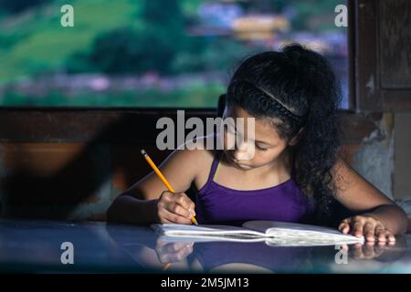 latina fille, brunette étudiant. petite fille se concentrant sur ses devoirs, s'appuyant sur une table en verre. Banque D'Images