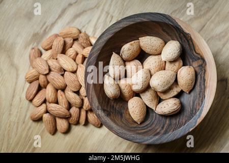 Amandes et amandes crues pelées dans une coquille dans un bol en bois sur fond en bois. Noix, nutrition et concept d'aliments crus Banque D'Images