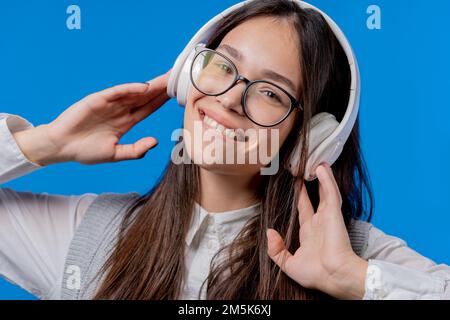 Un adolescent heureux étudiant écoutant de la musique, dansant avec un casque sur fond de studio bleu. Radio, technologie audio moderne sans fil, lecteur en ligne Banque D'Images