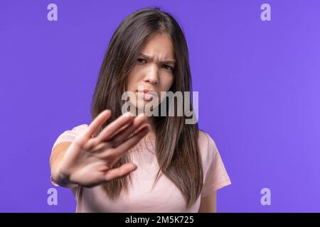 Jeune fille désapprouvant sans GESTE de signe de main. Refuser, rejeter, pas d'accord. Portrait de la jeune femme sur fond violet, délai Banque D'Images