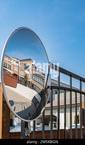 Miroir de sécurité extérieur convexe suspendu au mur avec une vue sur la route urbaine par les immeubles résidentiels. Miroir rond sur un poteau à h Banque D'Images