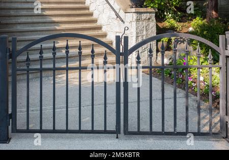 Porte noire en métal. Portes d'entrée de jardin en métal noir dans une clôture en brique. Grille en fer forgé noir de conception classique dans un jardin verdoyant Banque D'Images