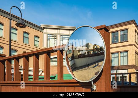 Miroir de sécurité extérieur convexe suspendu au mur avec une vue sur la route urbaine par les immeubles résidentiels. Miroir rond sur un poteau à h Banque D'Images