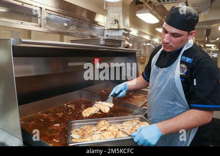 Spécialiste culinaire le Matelot de 1re classe Tim Arambula, de Fontana, en Californie, affecté au département d’approvisionnement de l’USS Gerald R. Ford (CVN 78), prépare le poulet dans la galley de l’arrière, au 22 mars 2022. Ford est en cours dans l’océan Atlantique en menant la certification de plate-forme de vol et la qualification de transporteur aérien dans le cadre de la phase de base sur mesure du navire avant le déploiement opérationnel. Banque D'Images