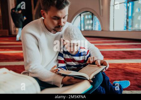 Prière musulmane père et fils dans la mosquée priant et lisant le livre holly Quran Together islamique Education concept Banque D'Images