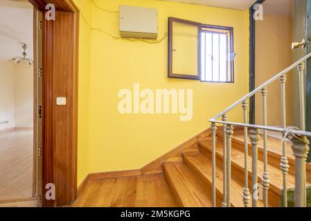 Ancienne maison avec un escalier avec marches en bois, une rambarde en fer forgé, des murs peints en jaune et un petit espace de rangement avec une porte verte Banque D'Images