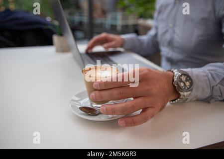 Un homme d'affaires boit du café tout en travaillant sur son ordinateur portable, gros plan de sa main Banque D'Images