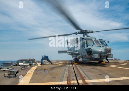 MER DE CHINE DU SUD (23 mars 2022) le marin Michael Blanchard, de Panama City Beach, Floride, place des cales et des chaînes sur un hélicoptère MH-60R Sea Hawk, affecté aux “rapaces” de l’escadron de frappe maritime d’hélicoptère (HSM) 71, sur le pont de vol du destroyer de missile guidé de classe Arleigh Burke USS Spruance (DDG 111). Abraham Lincoln Strike Group est en cours de déploiement prévu dans la zone d'exploitation de la flotte américaine 7th afin d'améliorer l'interopérabilité par le biais d'alliances et de partenariats tout en servant de force de réaction prête à l'emploi pour soutenir une région libre et ouverte d'Indo-Pacifique. Banque D'Images