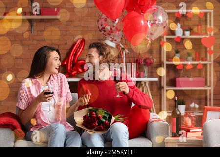 Joyeux jeune couple engagé qui boit du vin à la maison le jour de la Saint-Valentin Banque D'Images