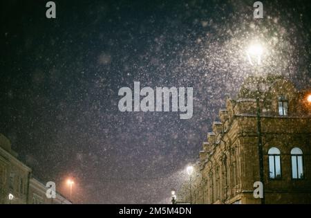 Lanterne lumineuse pendant la chute de neige sur la rue d'hiver de la ville le soir de Noël Banque D'Images