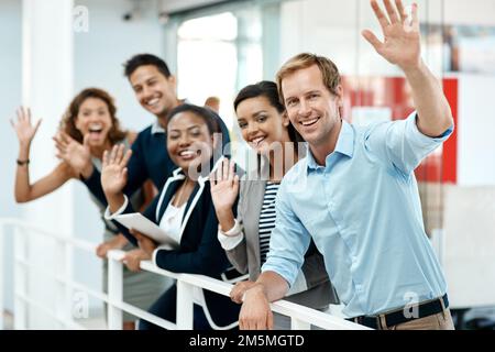 Votre entreprise est toujours Bienvenue. Portrait rogné d'un groupe de personnes en voyage d'affaires qui vous agite tout en se tenant dans leur bureau. Banque D'Images