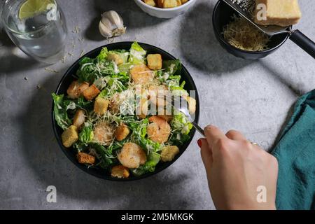 Gros plan de la femme mangeant de la salade César à la fourchette sur une table en marbre gris Banque D'Images