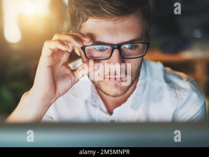 Concentration totale. un jeune designer travaillant sur un ordinateur tout en portant des lunettes dans le bureau. Banque D'Images