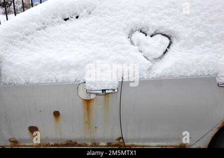 Signe d'amour en forme de coeur, dessiné sur une voiture enneigée. Forme de coeur dessinée à la main dans la neige fraîche. Symbole de l'amour en hiver Banque D'Images