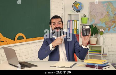 homme heureux avec la barbe calculant sur la calculatrice dans la leçon de mathématiques à l'école, les mathématiques Banque D'Images